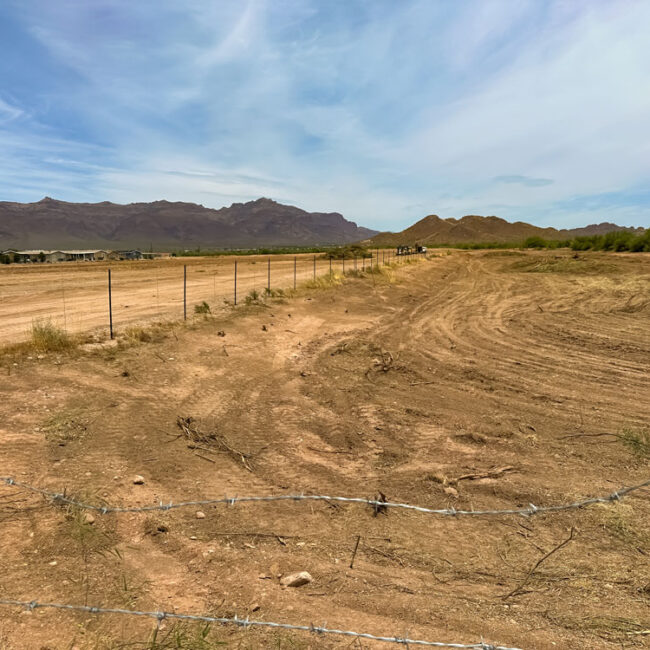 A dirt field with a fence and mountains in the background.
