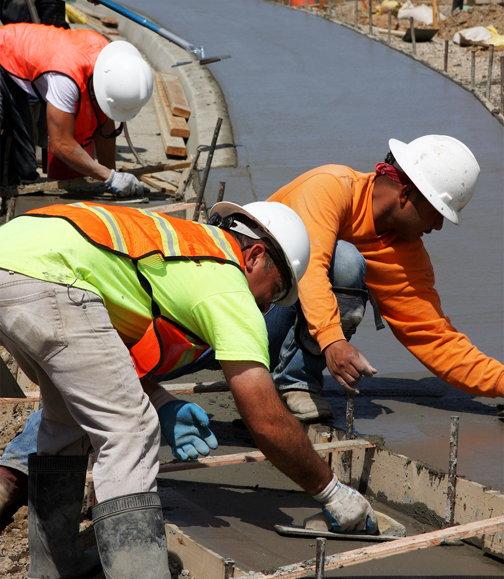 A group of construction workers working on a concrete sidewalk.