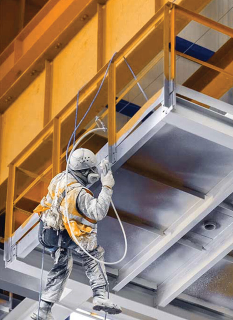 A worker is spraying a ceiling in an industrial building.