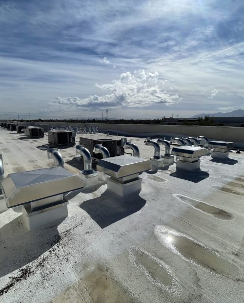Flat commercial building rooftop with multiple HVAC units and shiny metallic vents under a partly cloudy sky, mountains visible in the distance. Shadows and water stains are present—ideal for a laundry company like The Laundry Co seeking reliable facilities.