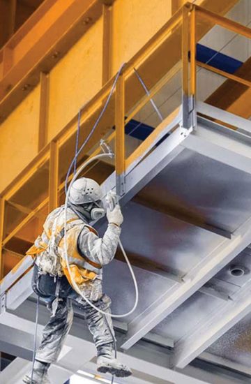 A worker is spraying a ceiling in an industrial building.